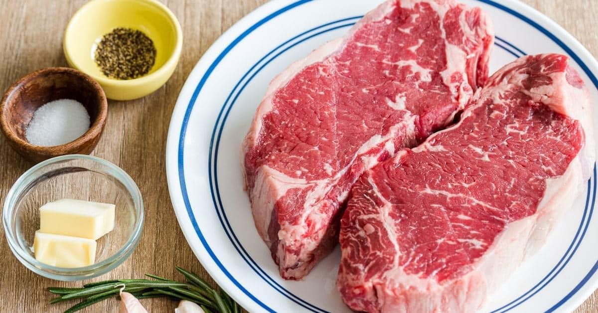 Two steaks on a plate with salt, pepper, butter, and rosemary